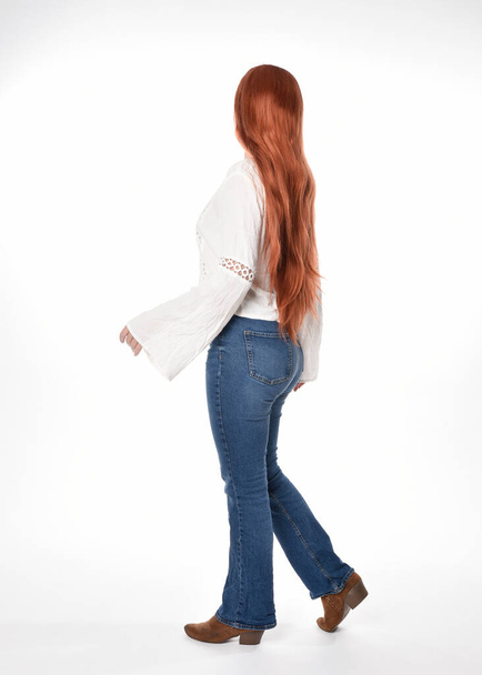 täyspitkä muotokuva kaunis nainen malli pitkät punaiset hiukset, yllään rento asu valkoinen pusero alkuun ja denim farkut, eristetty valkoinen studio tausta. Taaksepäin seisova asento, kävely pois kamerasta. - Valokuva, kuva