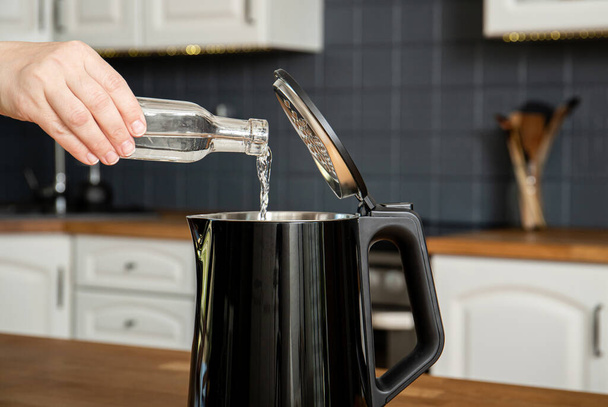 Woman pouring natural destilled acid white vinegar in electric kettle to remove boil away the limescale. Descaling a kettle, remove scale concept. Home kitchen background. - Foto, Bild
