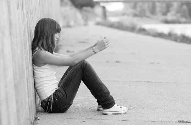 Samotna dziewczyna siedzi na betonie ziemi w środowisku miejskim - Zdjęcie, obraz