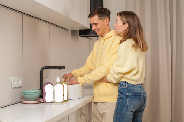 Прекрасна пара обіймає і миє посуд використовуючи посудомийну рідину з порожньою етикеткою
 - Фото, зображення