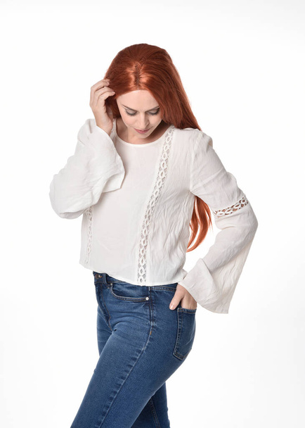  Close up portrait of beautiful woman model with long red hair, wearing casual outfit white blouse  top and denim jeans.  Posing with gestural arm poses, isolated on white studio background.  - Foto, Bild