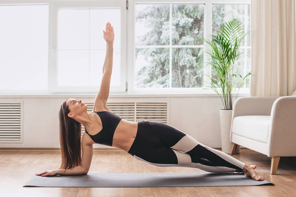 girl wearing shortwear standing in side plank on one hand at gym, training body core and balance, strengthening abs muscles. Fitness at home - Photo, Image