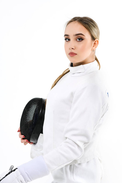Girl fencer with a sword on a white background. Portrait of a girl in a fencing costume with a mask and a sword. - Fotografie, Obrázek