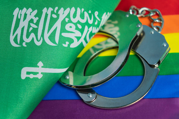 наручники, флаг Саудовской Аравии и флаг ЛГБТ. Проблема прав сексуальных меньшинств в стране. Концептуальный закон, запрещающий пропаганду ЛГБТ. нетрадиционные отношения и политическая концепция. - Фото, изображение