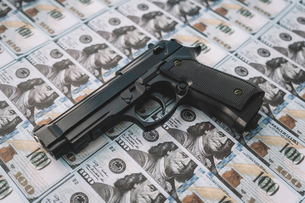 черная пушка на фоне наличных долларов. понятие преступных денег или наемной деятельности. Криминальный бизнес - Фото, изображение