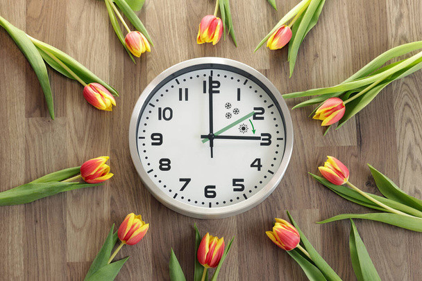Un orologio mostra tre ore. I tulipani sono in giro. Simbolo del cambio di tempo. Ora legale. Muovi le mani in avanti. La freccia verde indica la direzione di movimento delle mani. - Foto, immagini