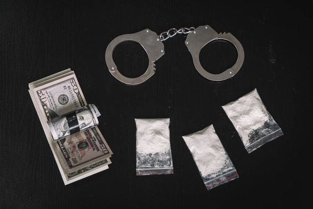 narkotický prášek v pytli peněz a pout na černém pozadí stolu. Koncept obchodu s drogami nebo obchodu s drogami. - Fotografie, Obrázek