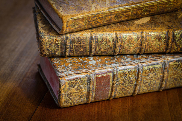 Pile of antique books with a leather cover and golden ornaments on a wooden table - Photo, Image