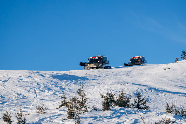 Tatry przejeżdżają przez zaśnieżone góry i oczyszczają tor dla snowboardzistów. Snowy zima jest wysoka na Ukrainie. Dragobrat pokryty śniegiem - Zdjęcie, obraz