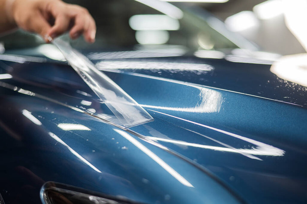 The master in the car service applies a protective armor film to the car body - Fotó, kép