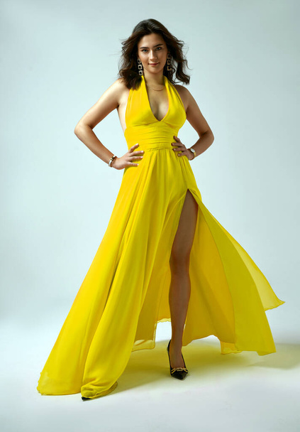 Sexy Fashion Model in Yellow Dress with Wavy Hair Style showing Leg over Gray Background - Valokuva, kuva