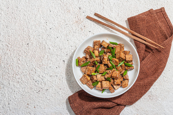 Gebratenes Teriyaki-Tofu mit Schalotten und Sesam. Gesunde vegane fleischlose Mahlzeit, reich an Proteinen und Kalzium. Trendy hartes Licht, dunkler Schatten, Gipshintergrund, Draufsicht - Foto, Bild