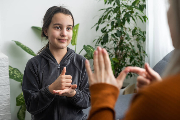 Nettes kleines Mädchen machen Handgeste Zeichensprache lernen mit Mutter oder Kindermädchen, lächelndes kleines Kind üben nonverbale Gespräche mit Lehrer zu Hause, Vorschulkind behinderten Kind haben Unterricht mit Tutor. - Foto, Bild