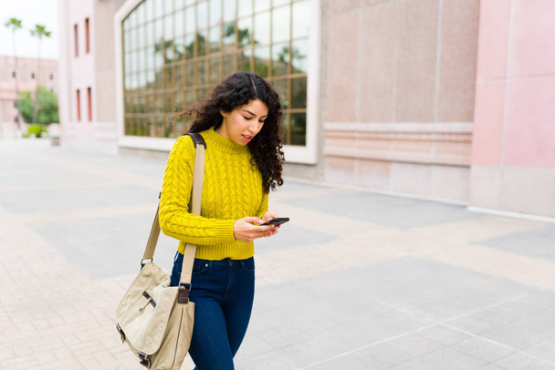 Hermosa mujer caucásica caminando por la calle de la ciudad y enviando mensajes de texto en su teléfono inteligente mientras viaja al trabajo por la mañana - Foto, imagen