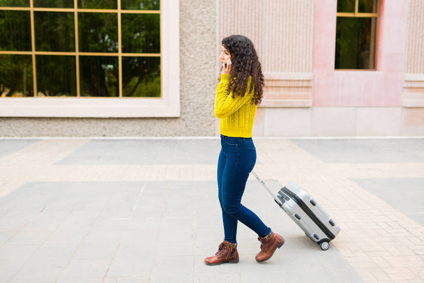 Zajęta młoda kobieta rozmawia przez telefon podczas spaceru na lotnisko w mieście za pomocą walizki przed podróżą służbową - Zdjęcie, obraz