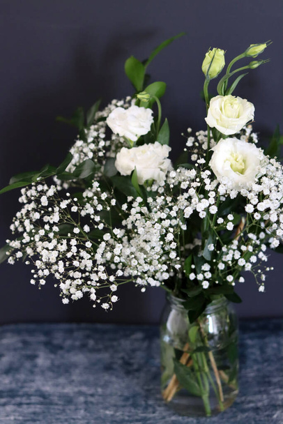 Composition simple nature morte avec des fleurs blanches de gypsophila dans un vase en verre. Fond sombre avec espace de copie.  - Photo, image
