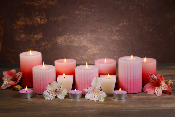 Beautiful candles with flowers on table on brown background - Foto, imagen