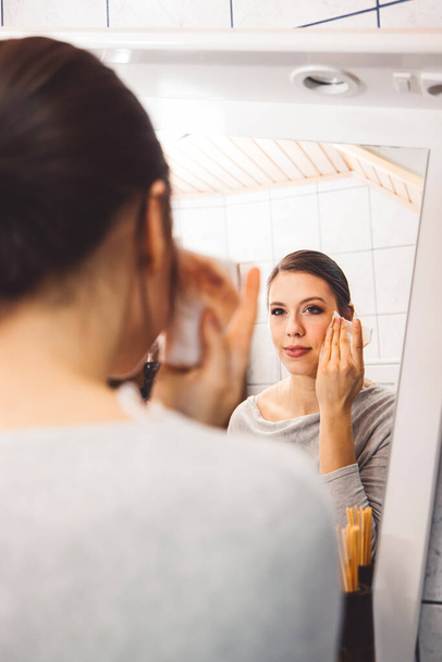 Beautiful young woman cleaning her face, removing make up with a cotton pad and micellar water. Skin care and beauty. Young beautiful woman cleaning her face. High quality photo - Foto, Bild