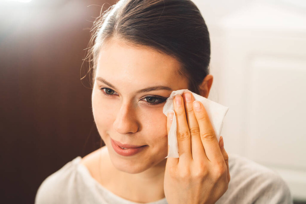Beautiful young woman cleaning her face, removing make up with a cotton pad and micellar water. Skin care and beauty. Young beautiful woman cleaning her face. High quality photo - Zdjęcie, obraz
