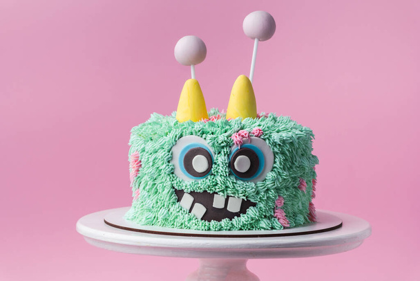 Monster Thema Kuchen auf dem rosa Hintergrund. Lustige Geburtstagstorte mit türkisfarbenem flauschigem Frischkäse-Zuckerguss. Gespenstisches Monstergebäck mit essbarem Fell. Fröhliche Halloween-Party - Foto, Bild