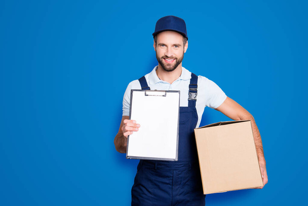 Portrait with empty place, copyspace of cheerful, attractive man having, carrying box in hands demonstrate clean paper in clipboard, looking at camera, isolated on grey background. - Photo, Image