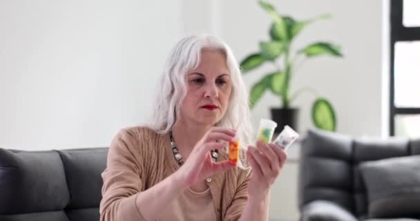 Ältere Frau mit grauen Haaren, die zu Hause Gläser mit Medikamenten anschaut und zu Hause den Titel eines 4k-Films in Zeitlupe vorliest. Vitamine für Menschen im Alter - Filmmaterial, Video