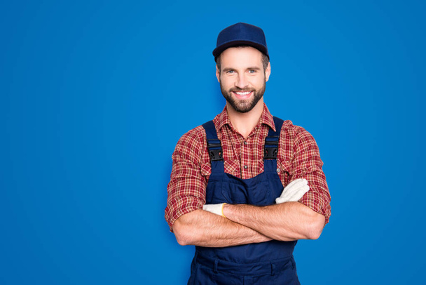 Portrait of handsome mechanic with stubble in blue overall, shirt having his arms crossed, looking at camera, isolated on grey background. - 写真・画像