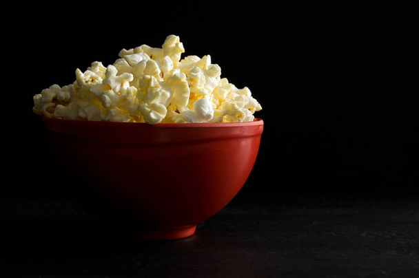 Sluiten Side View of Buttered Popcorn in een rode schaal geïsoleerd op zwarte horizontale - Foto, afbeelding