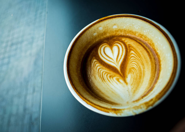 cup of hot latte coffee with love heart shape foam milk over dark background - Foto, Bild
