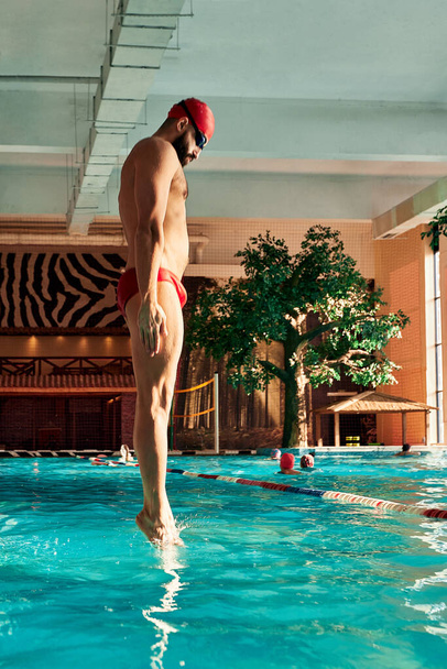 A male swimmer dives into the pool with his head into the water, the start of the swim in the pool - Fotografie, Obrázek