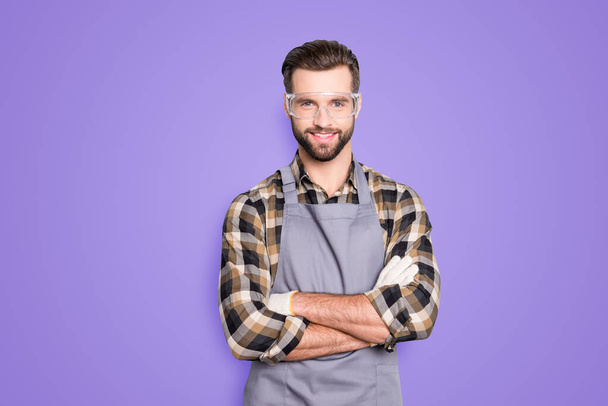 Portrait of attractive joyful carpenter with hairstyle in safety glasses looking at camera having his arms crossed standing over grey background. - Foto, immagini