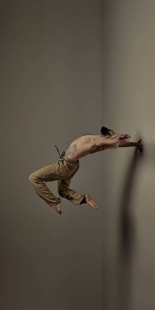 Strength. Sportive shirtless man training, doing stretching and yoga exercises against studio background. Levitation. Art of movement, male body aesthetics, health, sportive lifestyle concept - 写真・画像