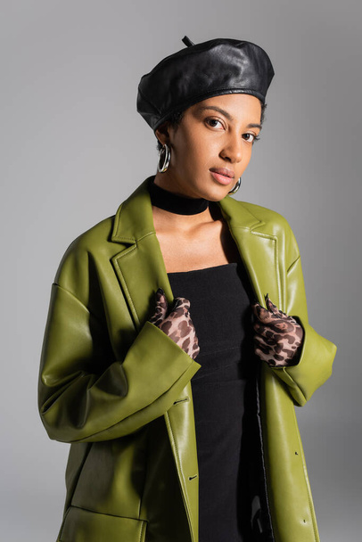 Stylish african american model in beret and leather jacket standing isolated on grey  - Foto, immagini