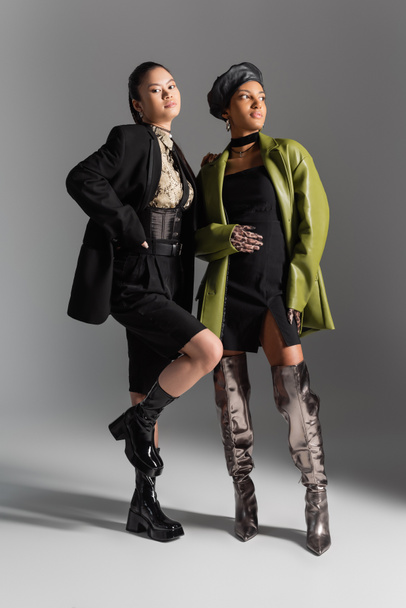 Full length of fashionable multiethnic models in jacket and coat posing on grey background - 写真・画像