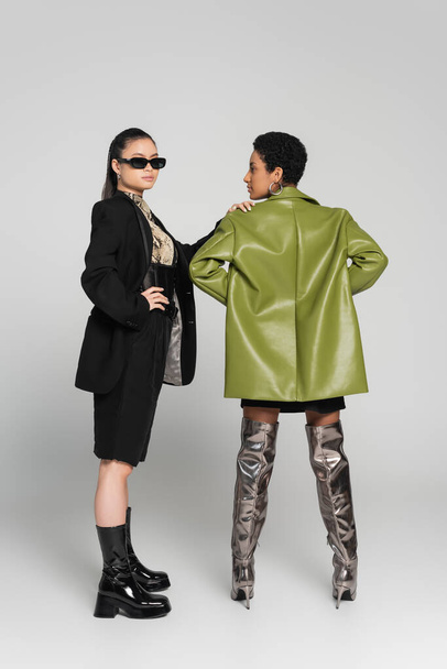 Longitud completa de modelo asiático de moda posando con amigo afroamericano sobre fondo gris - Foto, imagen