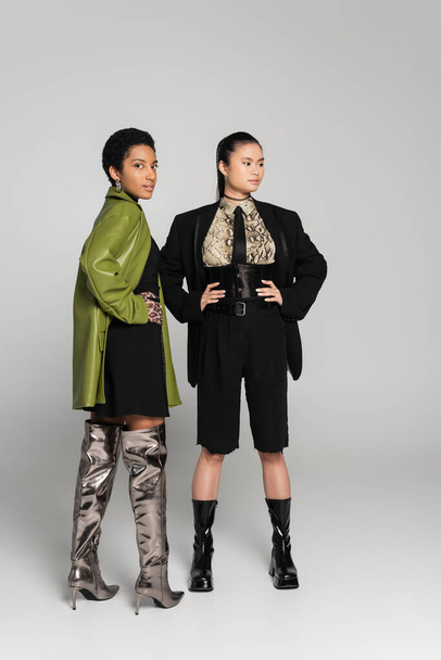 Stylish african american woman posing near asian friend in jacket on grey background - Photo, Image
