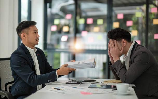 Sad and stressed Asian male office worker or businessman receives a complaint from his boss while working on his project with his team.  - Photo, Image
