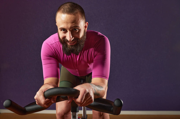 運動自転車で笑顔コピースペース暗い背景,運動自転車で心臓トレーニングを行う男,脂肪燃焼,減量,テキストのためのスポーツライフスタイルのコンセプトスペース. - 写真・画像