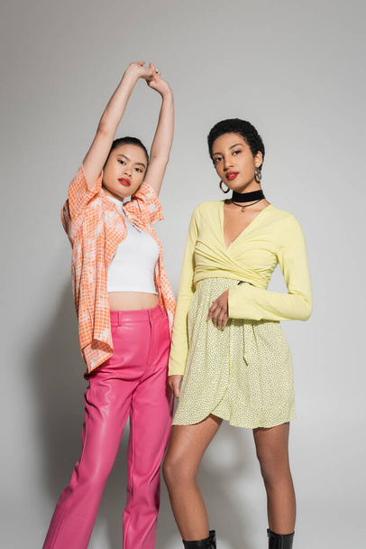 Stylish multiethnic models in bright outfit posing on grey background  - Фото, зображення
