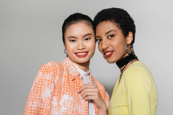 Mujeres multiétnicas de moda con maquillaje sonriendo a la cámara sobre fondo gris  - Foto, Imagen