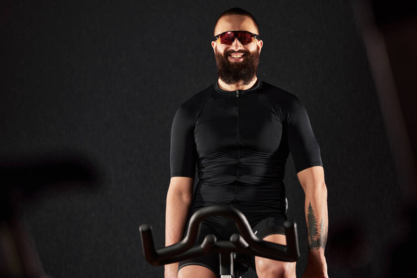 Man smiling on exercise bike copyspace dark background, man doing cardio workout on exercise bike, fat burning, weight loss, sport lifestyle concept space for text. - Photo, Image