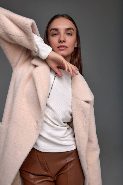 Beautiful fashionable woman in a cozy fur coat on a gray background positive girl posing at the camera in beautiful spring clothes. - Fotografie, Obrázek