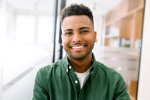 Close-up portrait of a happy indian young man with friendly wide toothy smile, latin guy wearing casual ggreen shirt looks into camera, employee profile photo - Φωτογραφία, εικόνα