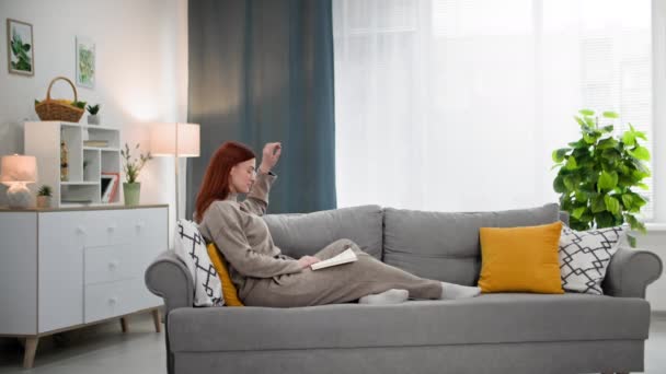 junge Frau mit Buch in der Hand verbringt Zeit damit, Literatur zu lesen, während sie zu Hause auf dem Sofa sitzt - Filmmaterial, Video