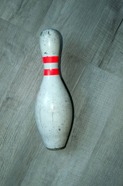 An old used bowling pin lays on its side on a grey floor. - Photo, Image