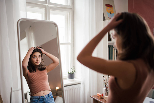 Young teenage girl looking in the mirror in the room. - Фото, зображення