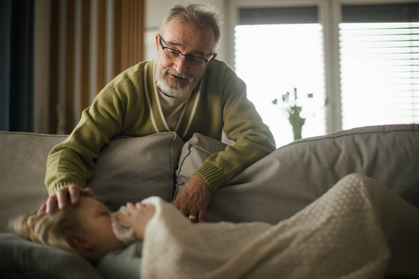 Senior man taking care of sick granddaughter. - Foto, afbeelding
