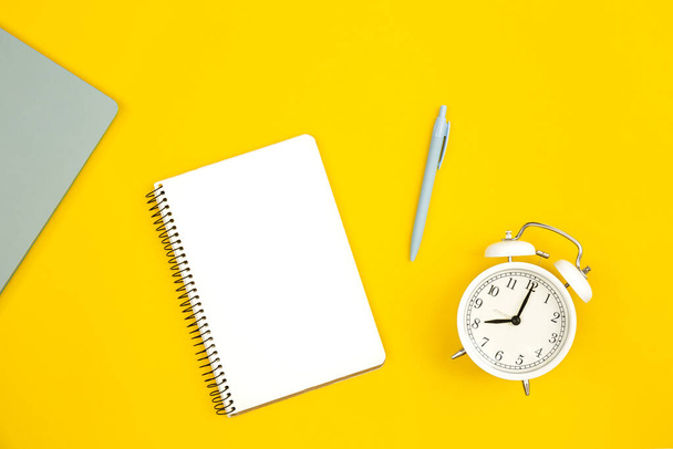 Reloj despertador blanco y bloc de notas en blanco sobre fondo amarillo, plano, espacio de copia. - Foto, imagen
