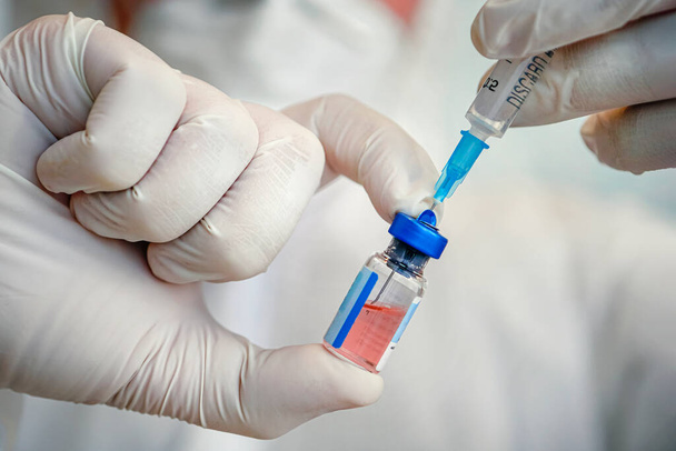 Un frasco de vacuna de cerca en la mano de un médico con guantes blancos sobre un fondo azul. - Foto, Imagen