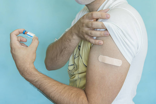 皮膚に傷やワクチンの注射後、若い男の腕の上に茶色の接着剤包帯.応急処置だ。医療、薬局、医療の概念。閉鎖だ。covid 19コロナウイルスに対する大量接種 - 写真・画像